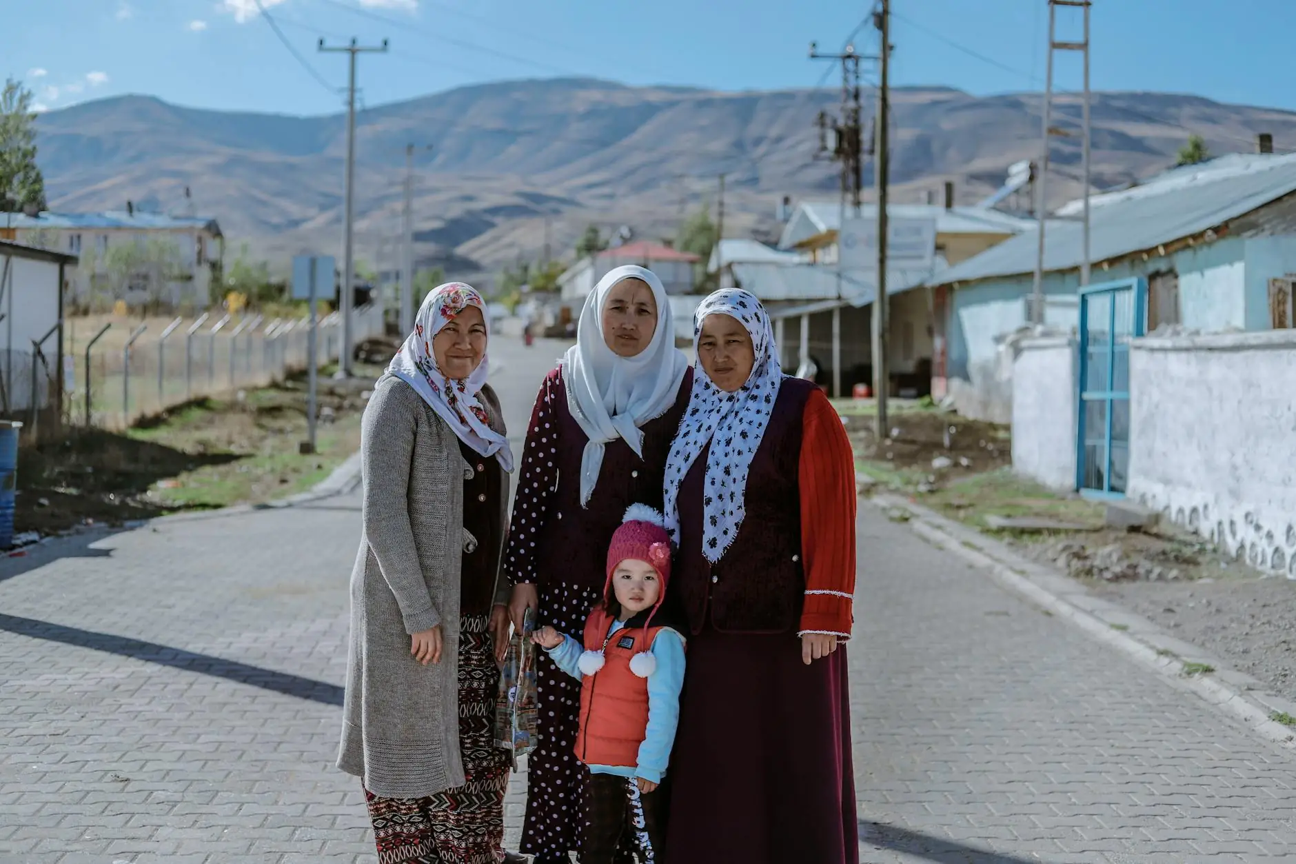 Women and a young girl standing on a village street with mountains behind them